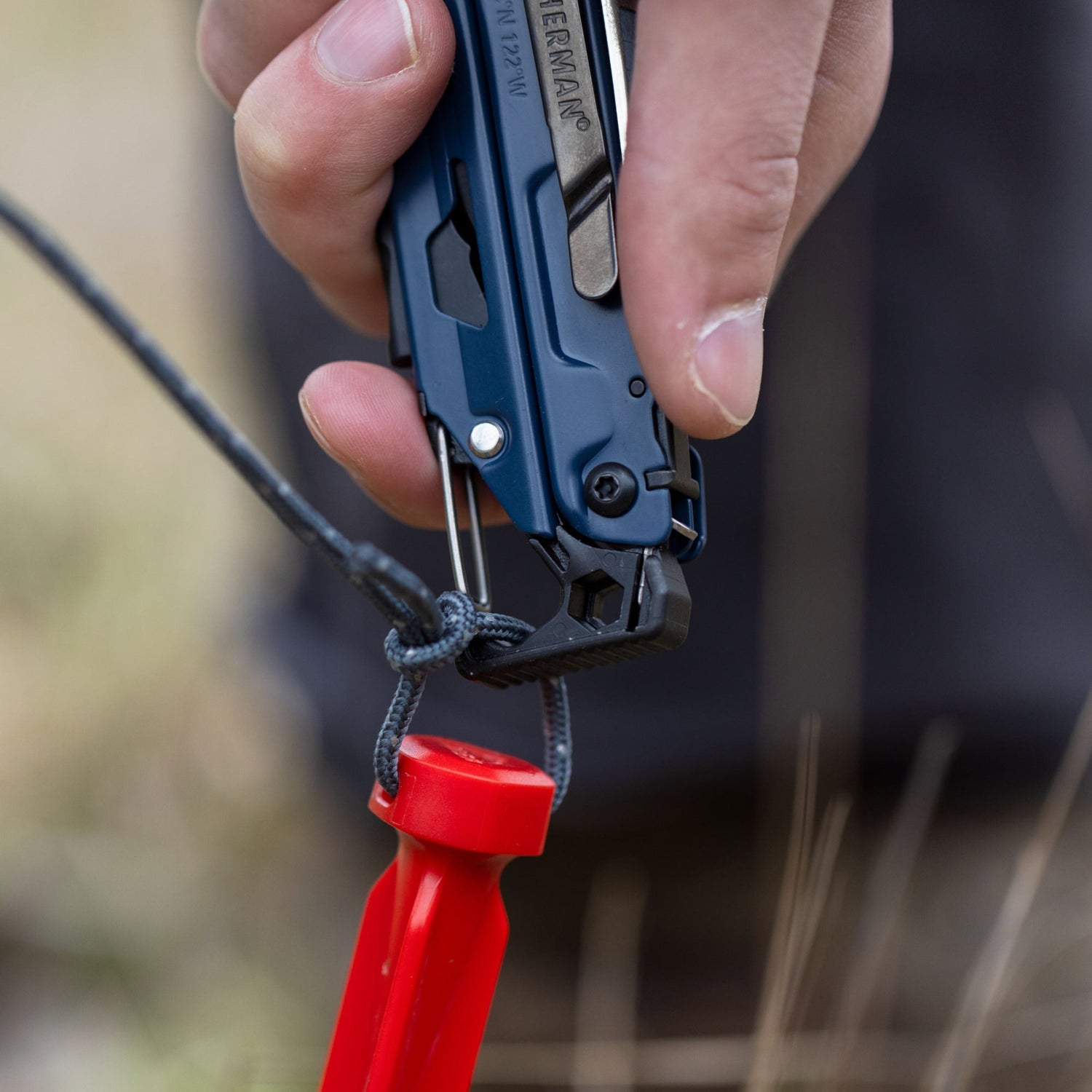 Person using the carabiner on a Nocturnal Leatherman Signal on a tent stake rope