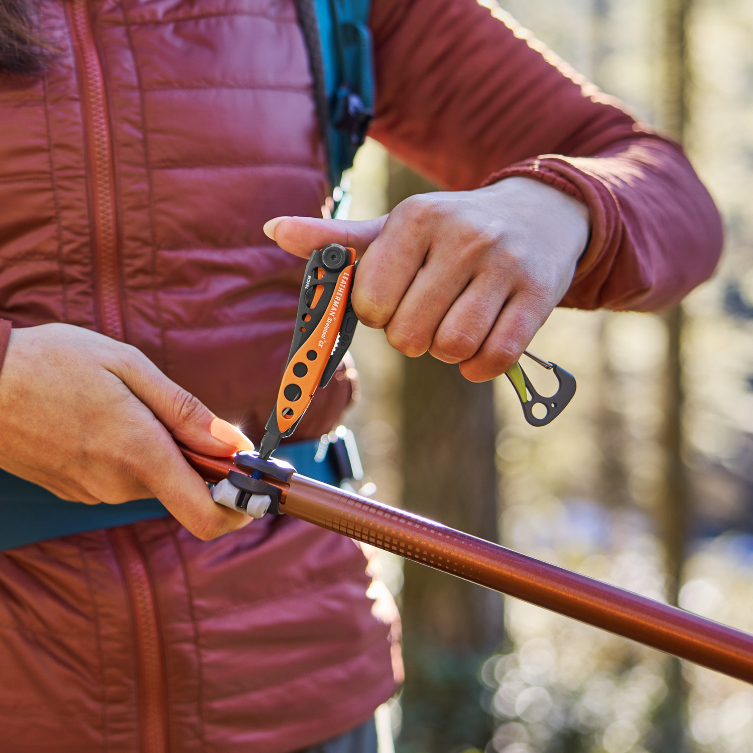 Person using an Aurora Leatherman Skeletool CX to adjust a hiking pole outdoors