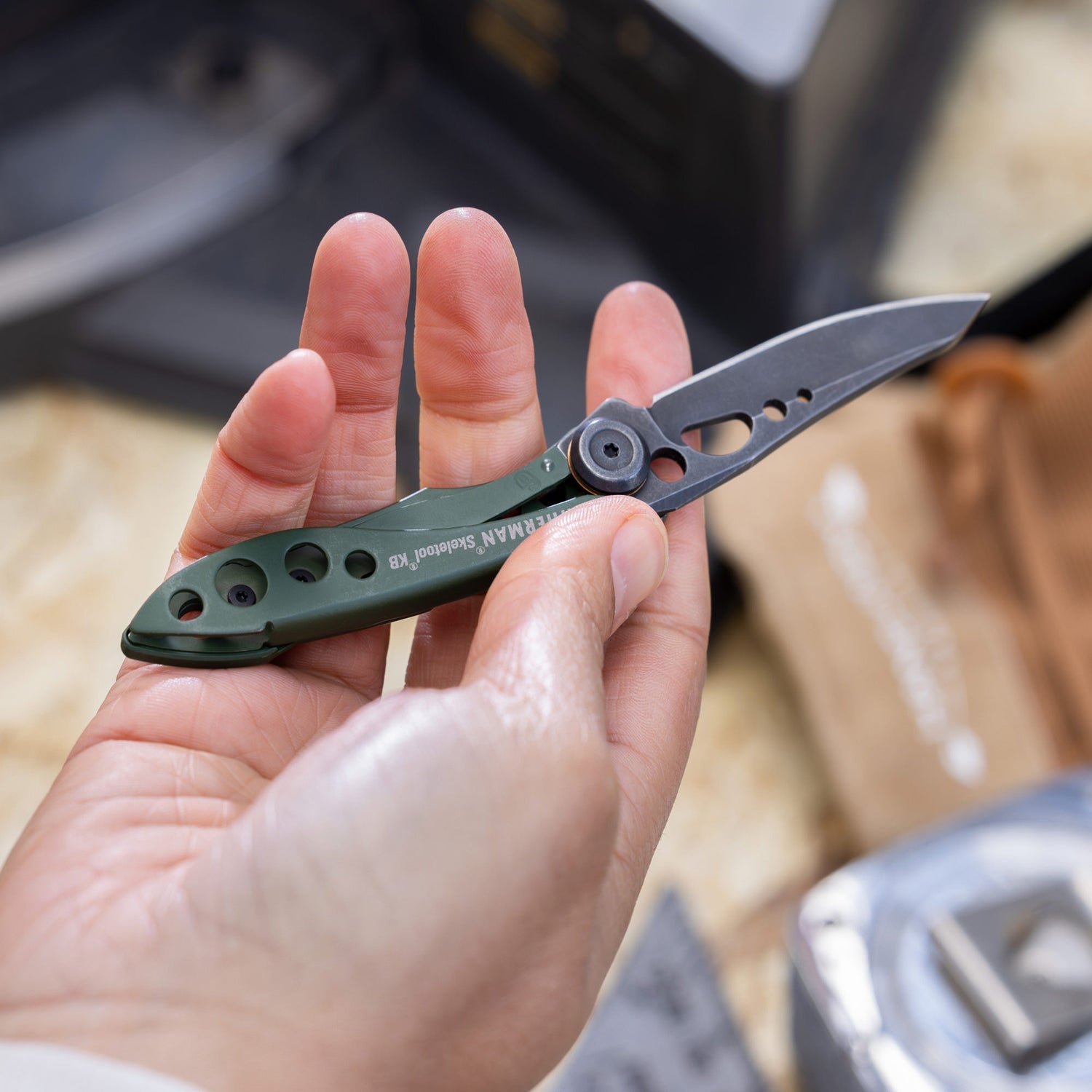 Hand holding an OD Green Leatherman Skeletool KB with the blade open
